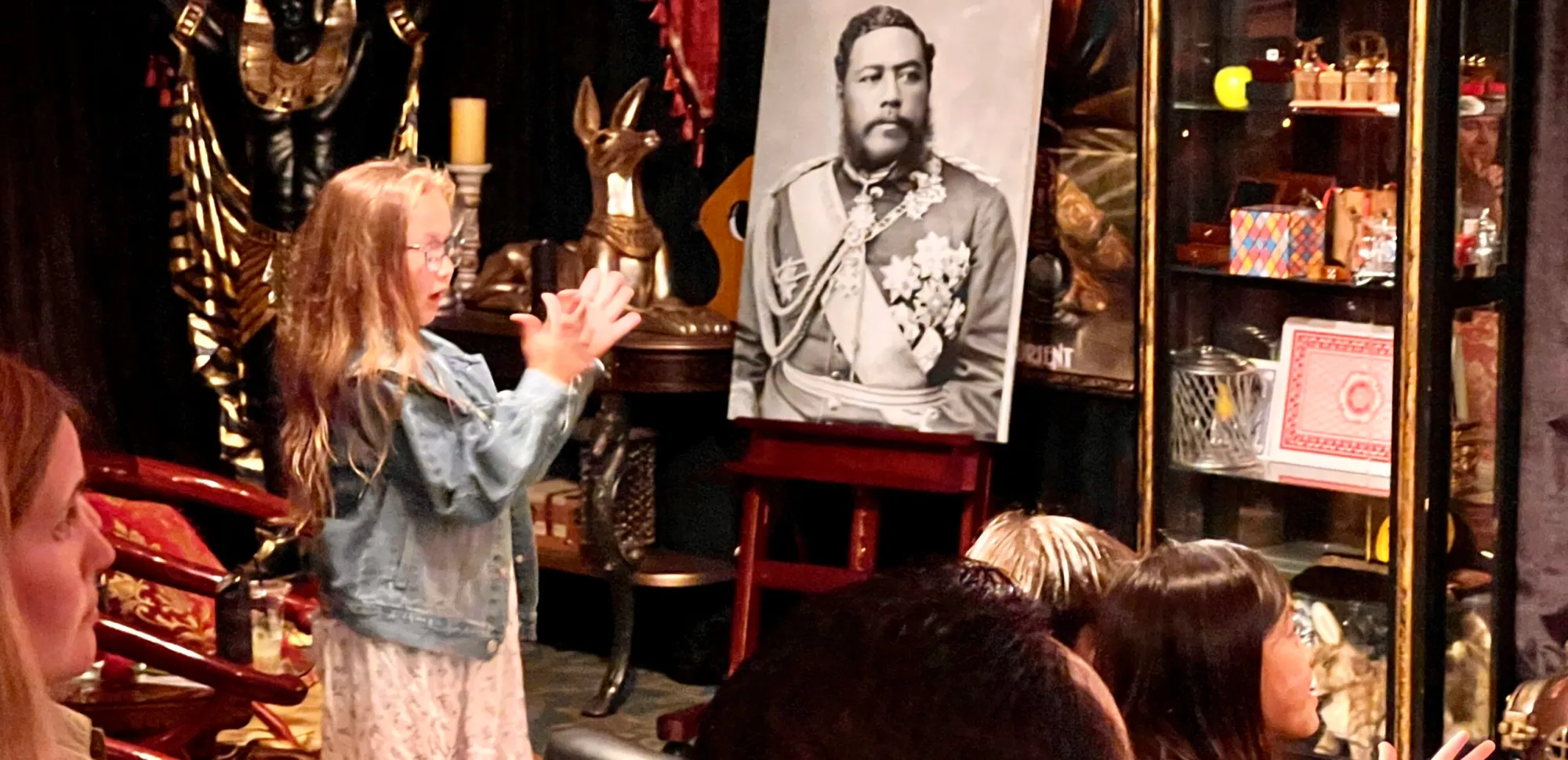 Young girl interacting with a magician, performing magic in front of an audience.