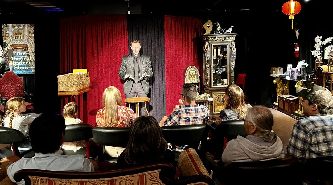 Magician performing a trick on stage for an audience at The Magical Mystery Show.