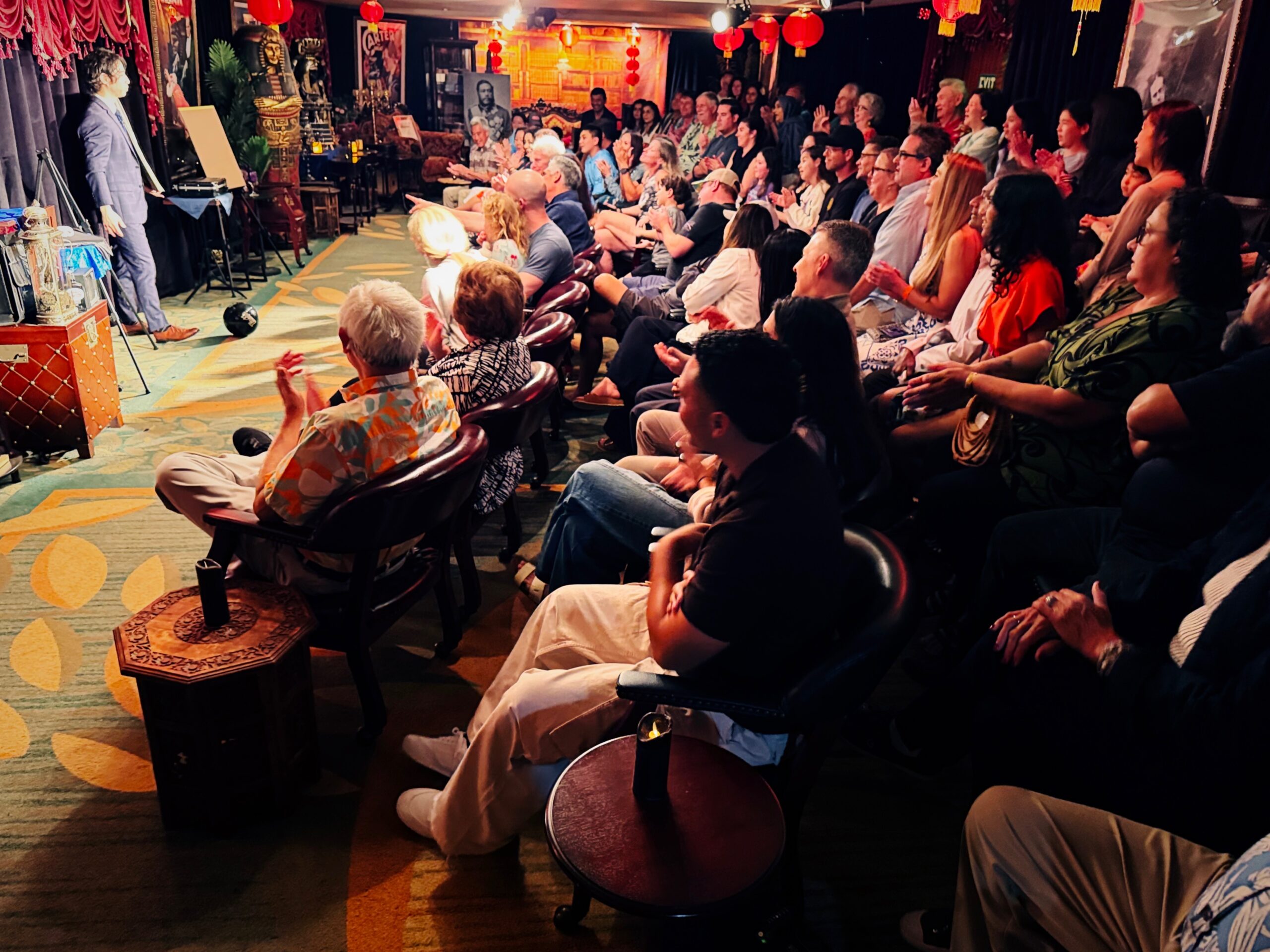 Magician performing on stage for a captivated audience, with guests clapping and reacting to the performance.