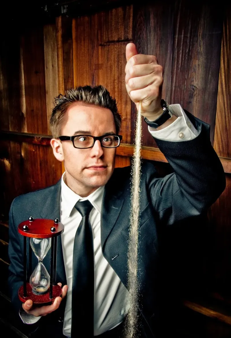 Magician holding an hourglass while letting sand fall from his hand, creating a magical effect during a performance.