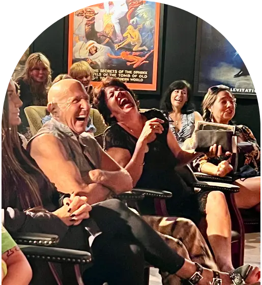 People sitting in chairs laughing with movie posters in the background.