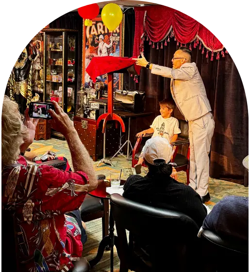 Magician performing levitation trick with a child on stage, audience watches and records with phones.