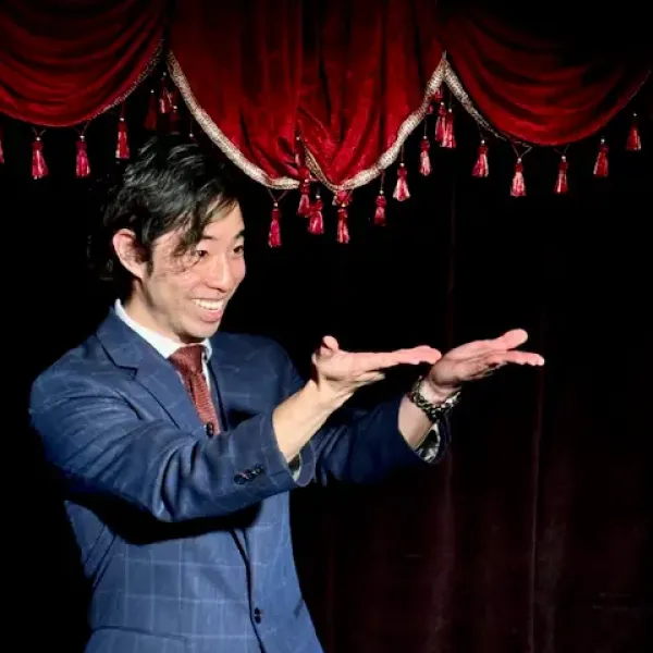 Man in suit performing with red curtain backdrop, gesturing with hands, smiling.