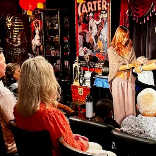 Magician performing a trick for an audience, with ornate decor and vintage posters in the background.
